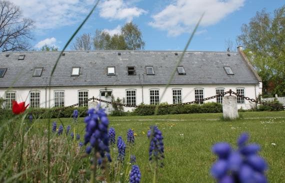 Beboerbygningen på Vibygård samt græsplæne og blomster en sommerdag med blå himmel