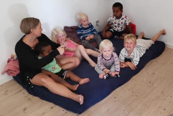 Kvinde der sidder på en madras på gulvet med fem børn