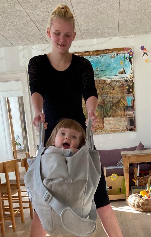 En smilende mor, der gynger sit grinenede barn i en slynge